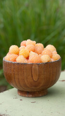 Frambuesas amarillas en cuenco marrón sobre fondo verde de arbusto de hierba en jardín