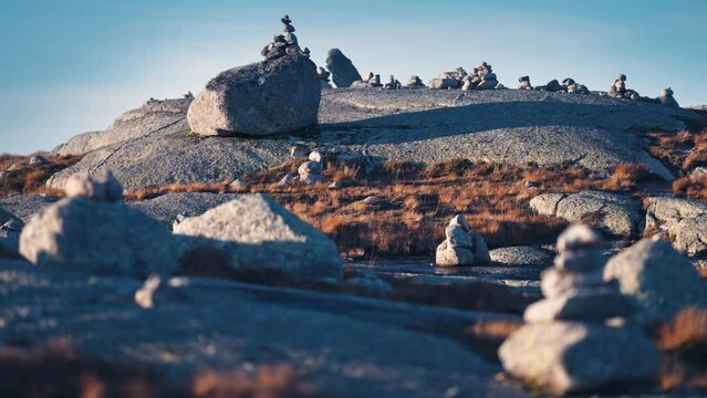 A meditation stone garden in the stark Nordic landscape. Small stone cairns are scattered around. Moss, lichen, and withered grass cover the stones. Slow-motion, pan right.