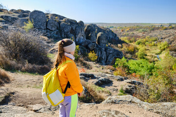 little girl with a backpack standing on a mountain top at the day time