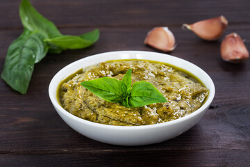 Pesto sauce in a plate and fresh basil leaves with garlic. dark wooden background, copy space.