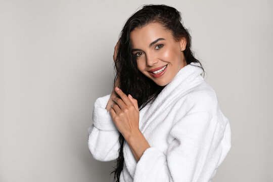 Beautiful young woman wearing bathrobe on light background