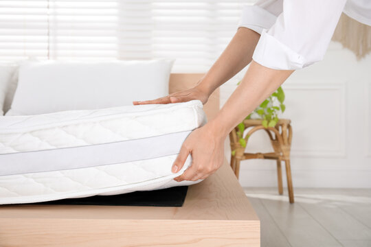 Woman putting soft white mattress on bed indoors, closeup