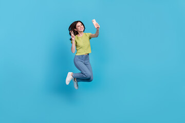 Fototapeta na wymiar Full size photo of cool young brunette lady jump do selfie wear t-shirt jeans shoes isolated on blue background
