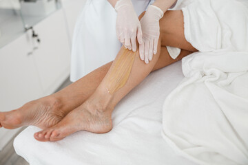 Woman client having hair removal procedure on leg using sugaring paste in beauty salon