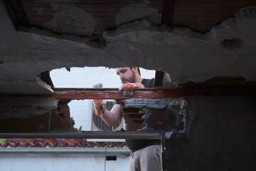 Young man pulling the ceiling of a house down using a mallet.