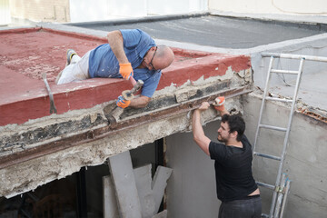 Two masons removing old metal beams in a construction house.