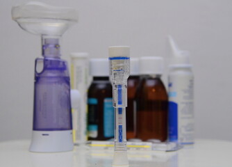 Covid-19 test kit for detecting IgM/IgG antibodies and immunity in 15 minutes. Two stripes - positive. In the background are medicines, syrups, a thermometer, an inhaler