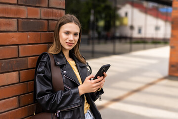 Business woman uses by mobile phone outdoors, professional woman walking along the street