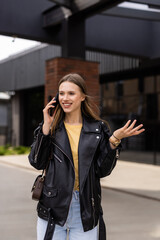 Cheerful young woman looking down on street while talking over smartphone. Smiling girl walking on street and talking on phone.