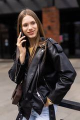 Cheerful young woman looking down on street while talking over smartphone. Smiling girl walking on street and talking on phone.