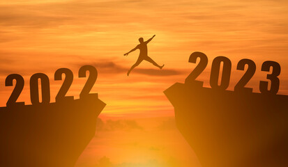 Concept Happy new year 2023 Silhouette image of happy man jump from 2022 up to 2023 on beautiful sky sunrise.