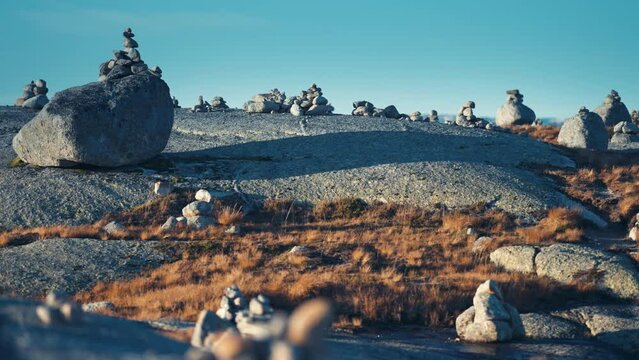 A stone garden in the stark Nordic landscape. Stone cairns are scattered around rocky terrain. Moss, lichen, and withered grass cover the stones. Slow-motion, pan right.