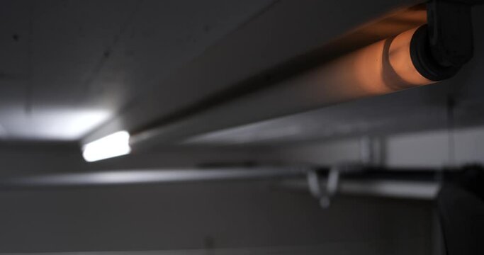 Broken neon-light tube flickering on a ceiling wall. Close up shot, real time, no people