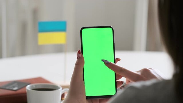 Use green screen for copy space closeup. Chroma key mock-up on smartphone in hand. Woman holds mobile phone. On the table is the flag of Ukraine.