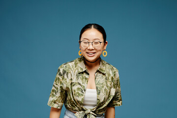Minimal portrait of Asian teenage girl wearing eyeglasses and smiling over blue background, copy...