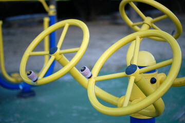 Close-up of colorful yellow and blue spinning metal wheel toy at a playground.