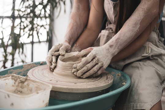 Man's hand draw heart on woman's hand with white clay. Studio on production of clay tableware love and tender. Work on potter's wheel. Side view. Concept of creative, skill and handmade.