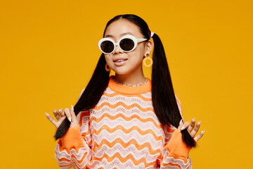 Waist up portrait of teenage Asian girl with pigtails wearing white sunglasses over vibrant yellow...