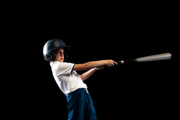Studio shot of sportive kid, beginner baseball player in sports uniform playing baseball isolated on black background. Concept of sport, achievements, competition