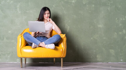 Image of beautiful young Asian woman sitting on yellow armchair