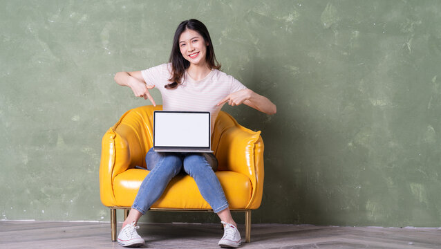 Image of beautiful young Asian woman sitting on yellow armchair