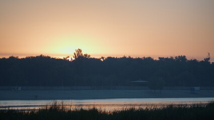 Fototapeta na wymiar Dark silhouette lush forest illuminated soft light sundown. Calm orange sunset