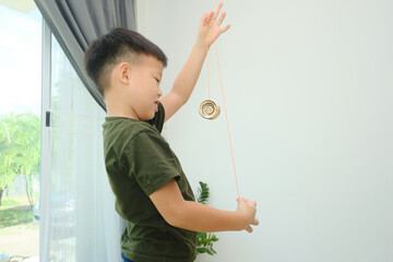 Cute little Asian school boy child having fun learning how to play with a yo-yo toy alone in living...