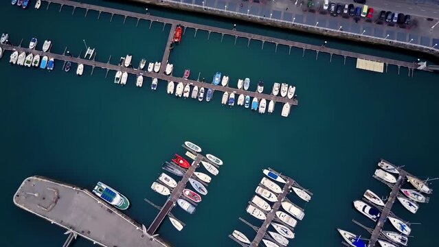 overhead drone shot over the port of Gijón in Spain where we see a large number of boats and yachts parked during a dark day with the blue and green of the sea that contrasts with the boats