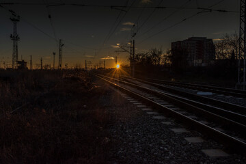 Plakat A scenic sunset over rail tracks near a station.