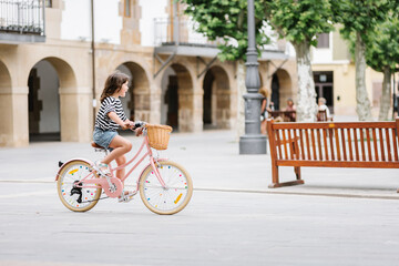 Fototapeta premium elementary caucasian girl rides in the square on a bicycle