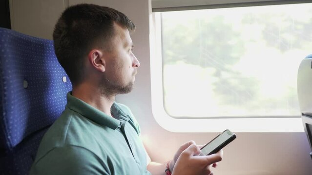 Man using mobile phone on a high speed train. Male on mask face protection, use smartphone and keep social distancing while commuting in public transport. Travelling by train with coronavirus.