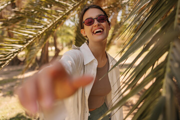 Cheerful young caucasian girl laughs walking in tropical park among palm trees. Brunette wears...