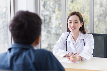 Obraz premium Asian professional woman doctor who wears medical coat talks with a man patient to consult and suggest healthcare information to him at the examination room in the hospital.