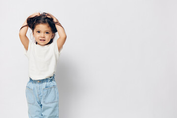funny, cute, little girl stands in a white T-shirt on a light background and raises her hair on her...