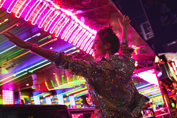 Naklejka premium Stylish woman wearing jacket with shining sequins on the city street with neon lights