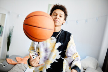 Waist up portrait of young teenage boy playing with basketball ball at home and smiling to camera