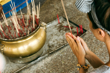 Young female tourist praying in buddhist temple in front of censer.