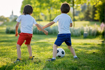 Two cute little kids, playing football together, summertime. Children playing soccer
