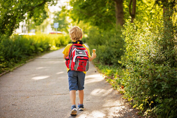 Adorable kid in colorful clothes and backpack, walking away and eating ice cream on a sunny summer afternoon, warm day