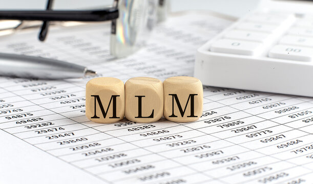 wooden cubes with the word MLM Multi-Level Marketing on a financial background with chart, calculator, pen and glasses, business concept.