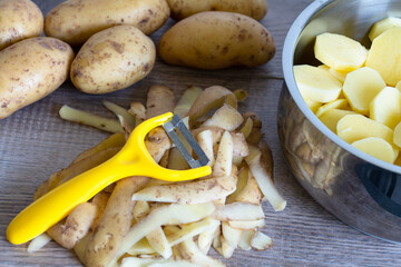 Gelber Pendelschäler, Kartoffelschalen und Kartoffelscheiben im Topf