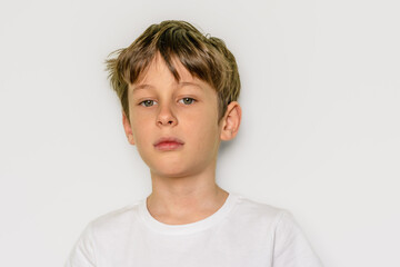 The child confidently looks directly into the camera . Portrait of a white Caucasian 9-year-old boy in a white T-shirt. Place to copy