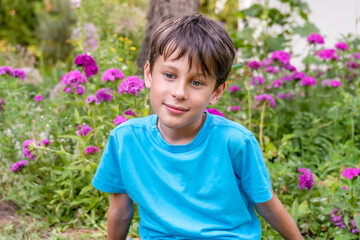 Portrait of a 9-year-old boy in a blue T-shirt among flowers in the garden