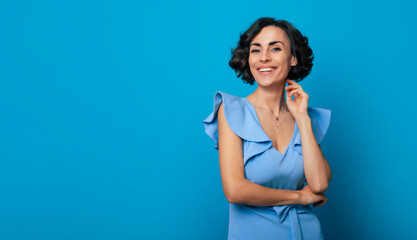 Close-up photo of a charming healthy woman in a blue dress, who is looking in the camera and smiling, while standing and posing isolated on blue background - Powered by Adobe