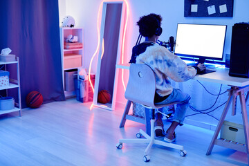 Wide angle angle portrait of teenage boy recording podcast at night in room with blue neon...