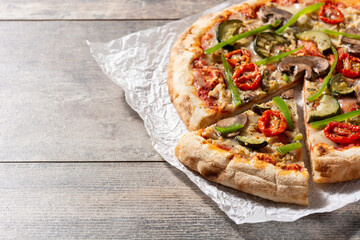 Vegetarian pizza with zucchini, tomato, peppers and mushrooms on wooden table. Copy space