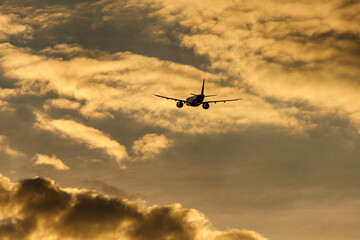 Silhouette of an airplane flying at sunset clouds.