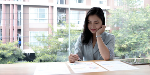 Beautiful Asian businesswoman analyzes charts using laptop calculator at the office.