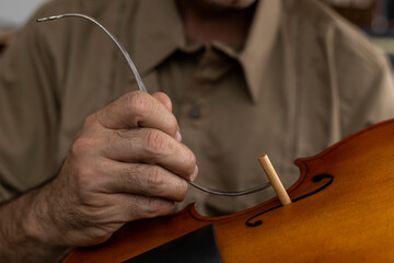 Latin American luthier placing a sound post between the top and the bottom of the violin. Stringed instruments concept - obrazy, fototapety, plakaty