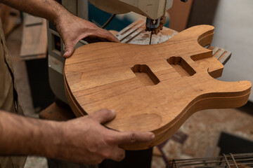 Close-up of unrecognizable Latin American luthier making an electric guitar with a saw. Stringed instrument construction concept